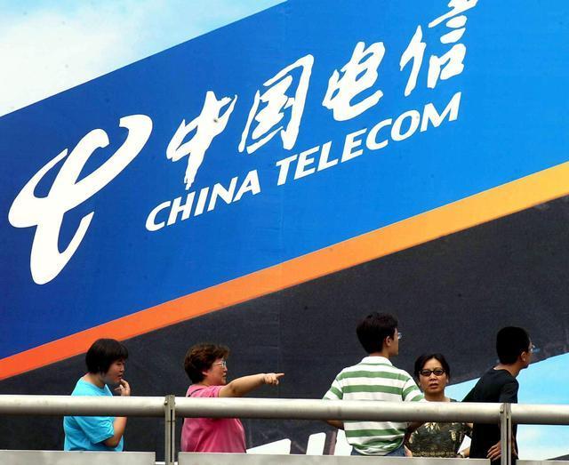 Pedestrians walk under a giant China telecom billb